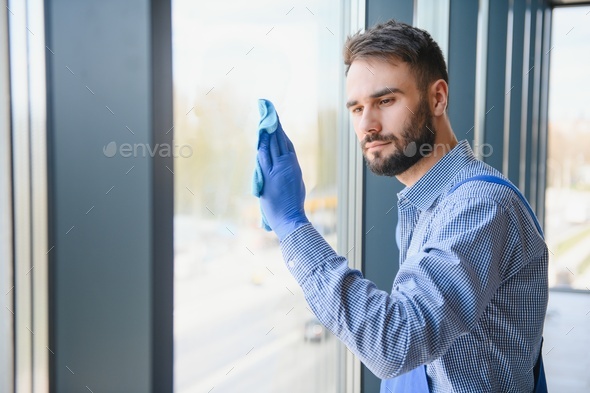 Male professional cleaning service worker in overalls cleans the windows and shop windows