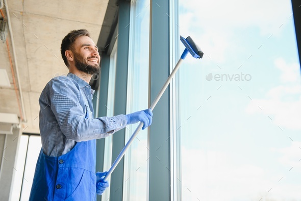Male professional cleaning service worker in overalls cleans the windows and shop windows