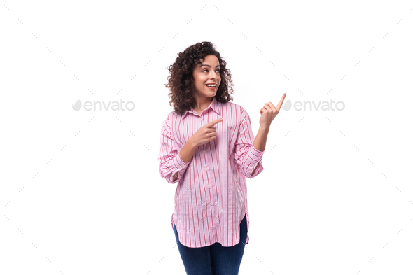 young pretty lady with curly black hair in a pink blouse points her hand to the side