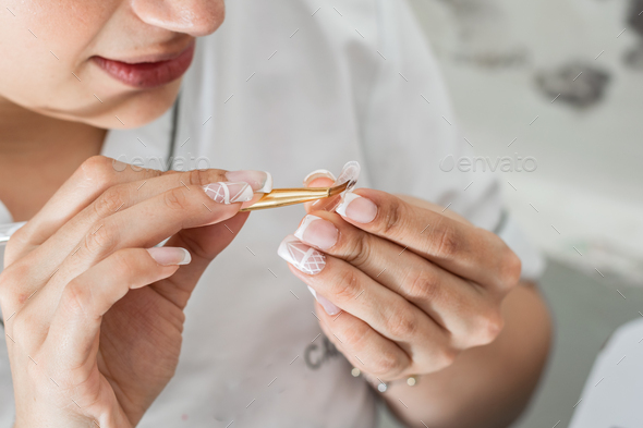 latina woman manicurist, carefully applying the special liquid gel with a brush on a false nail