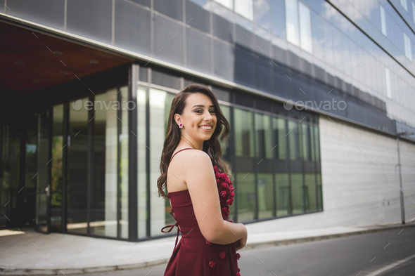 Attractive Caucasian Female Wearing An Elegant Burgundy Dress On Background Of A Building Stock