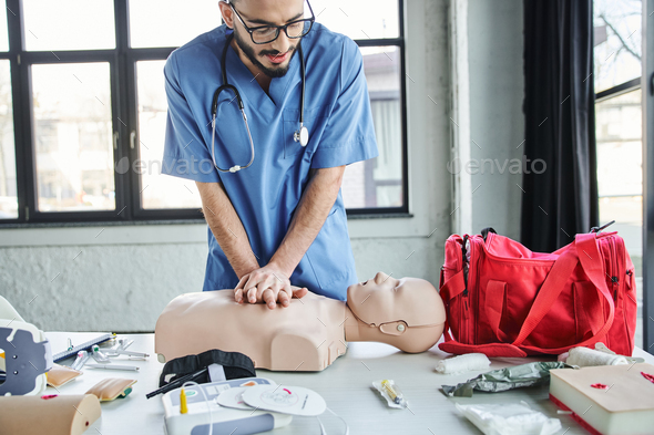 young professional paramedic practicing chest compressions on CPR manikin near red first aid bag,