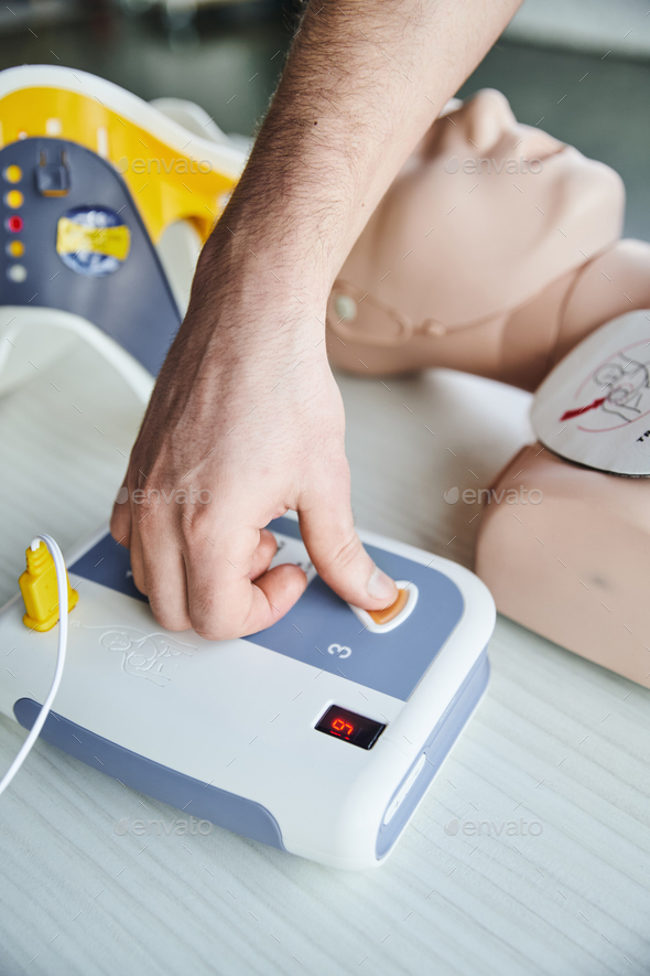 partial view of healthcare worker operating automated defibrillator