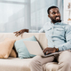 african american freelancer sitting on couch in living room and looking away - PhotoDune Item for Sale