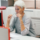 Serious middle-aged businesswoman gray-haired looking at monitor, sitting at office desk.  - PhotoDune Item for Sale