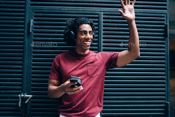 Smiling hipster guy in bluetooth earphones enjoying playlist entertainment gesturing in city