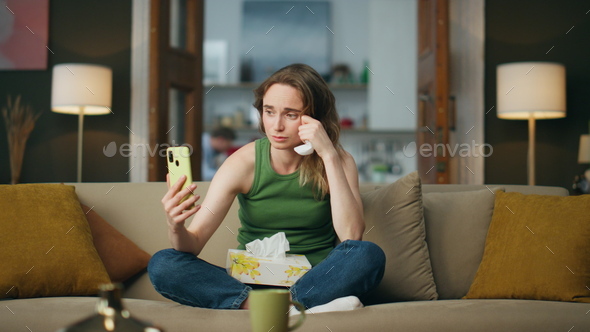 Depressed woman phone calling couch interior. Sad girl holding napkin suffering