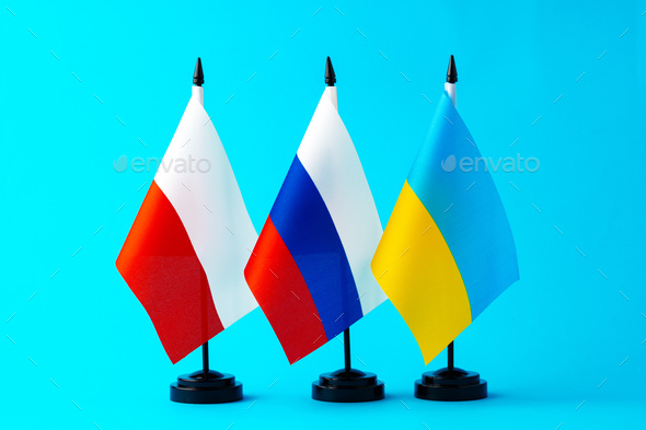 Three small flags of Russia, Ukraine and Poland on flagpoles on blue background