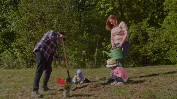 Parents with Two Children Planting and Watering a Tree in the Park alt