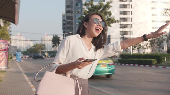 young Asia businesswoman hailing on road catching taxi and holding smart phone while. alt
