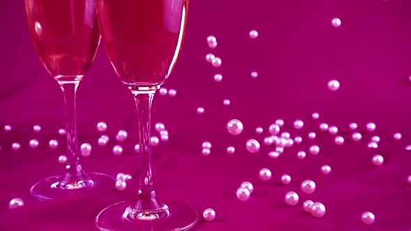 Falling white pearls next to wine glasses on a purple background. Slow motion. alt