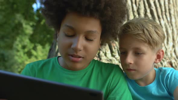 Male Friends Scrolling Tablet Application Sitting Outdoors Together, Technology