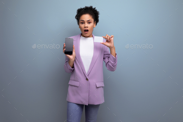 young well-groomed latin secretary woman with fluffy hair dressed in a lilac jacket hold bank card