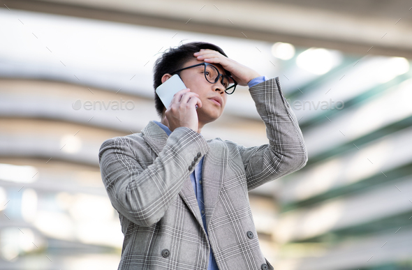 Asian businessman frowns at his phone during challenging call outdoor