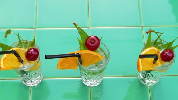 Refreshing summer drinks in crystal glasses leaves cherry orange on green tile background Cocktails