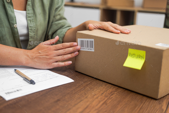woman affixes a Return sticker, with a barcode, to cardboard box, online shopping refund process.