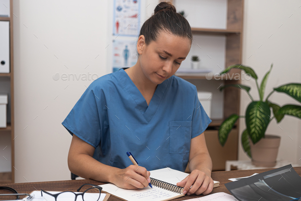Female practitioner in blue medical uniform works with medical documentation sitting in office