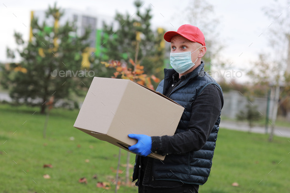 Delivery man in gloves and mask holds box on yellow background