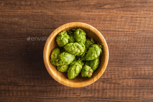 Green hops crop in bowl on wooden table. Top view.