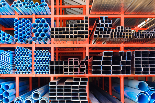 Various sizes of many carbon steel rectangular tubes with blue PVC water pipes on storage shelf