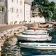 Row of fishing boats moored at the Perast pier against the backdrop of  ancient stone houses at the Stock Photo by Nadtochii