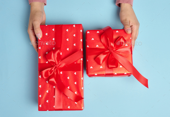 Female hand hold a box wrapped in red paper and tied with a red