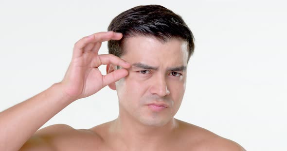 Beauty shot of young Hispanic man checking wrinkles on his face in white isolated background