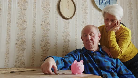 Mature Caucasian Man Puts Coin Into the Piggy Bank Wife Standing Beside Savings Concept alt