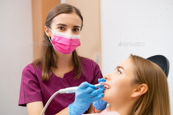 A dentist is performing a teeth grinding procedure on a lovely woman to enhance her smile