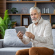 Senior gray-haired man sitting on the sofa at home, using a tablet, talking on a video call and - PhotoDune Item for Sale