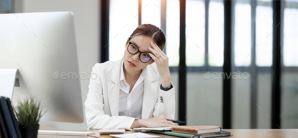 Young busy stressed upset Asian businesswoman feeling tired frustrated, sitting at office desk.