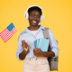 Happy young african american woman student in wireless headphones, with books, flag of USA - PhotoDune Item for Sale