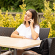 A young, beautiful, modern woman is talking on the phone on the terrace of a cafe - PhotoDune Item for Sale