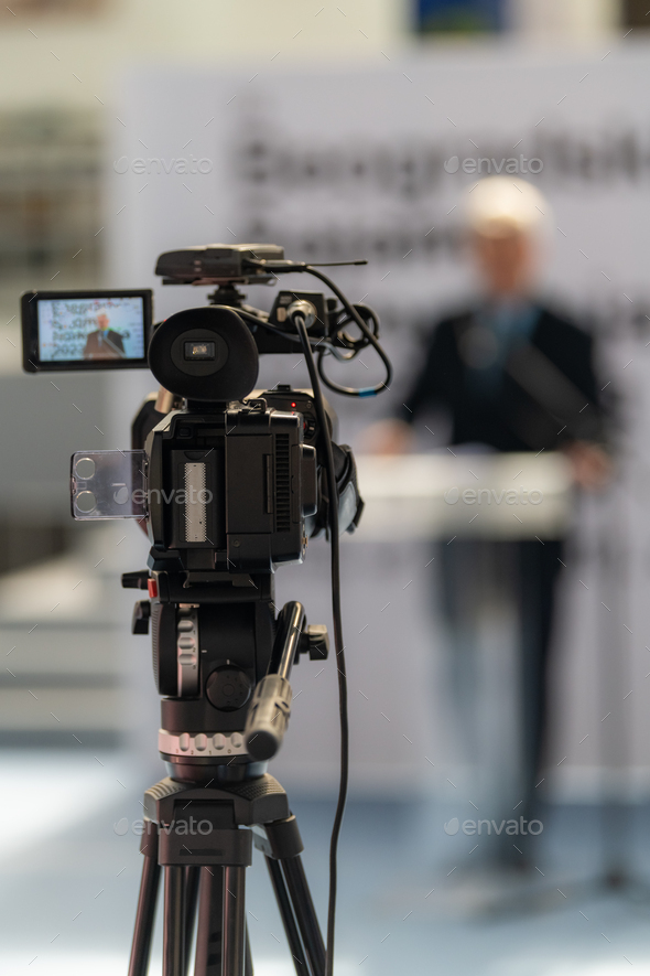 TV camera records a compelling male speaker on stage, delivering impactful insights on fair