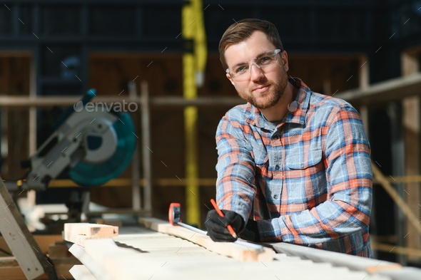Skilled cabinet maker cutting wood board with electric circular saw at woodworking sawmill.