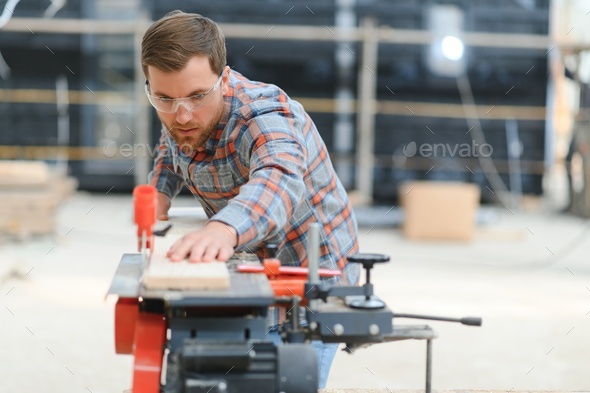 Skilled cabinet maker cutting wood board with electric circular saw at woodworking sawmill.