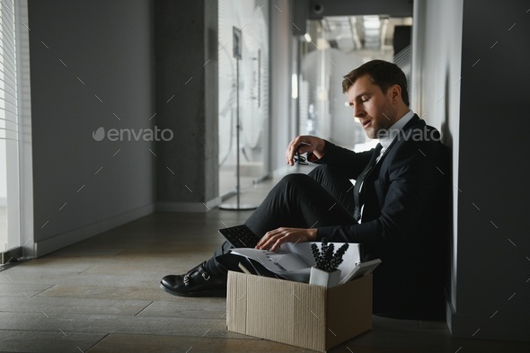 Sad fired businessman sitting outside meeting room after being dismissed.