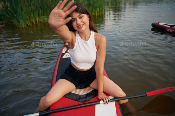 Covering face with hand, don\'t want to be photographed. Young woman is on sup boards in the lake