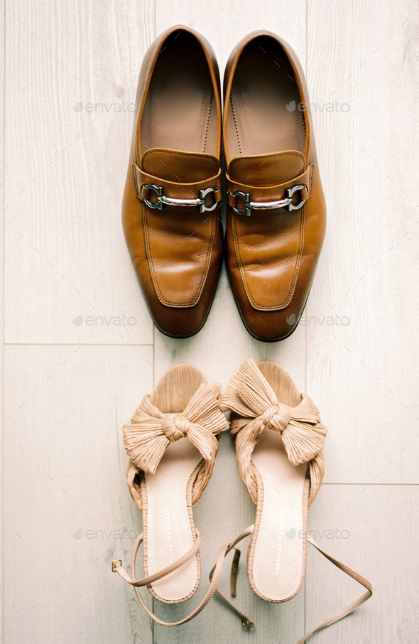 Bride and groom shoes stand opposite each other on a light laminate floor. Top view