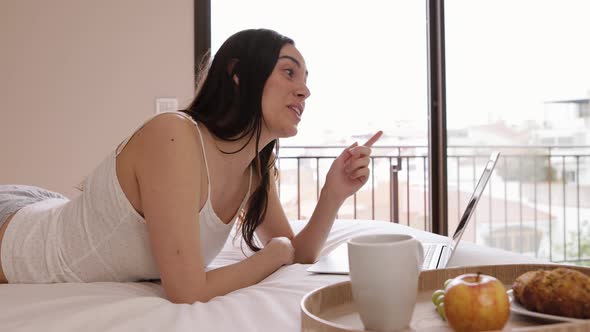 Smiling woman having online call on laptop chilling on bed alt