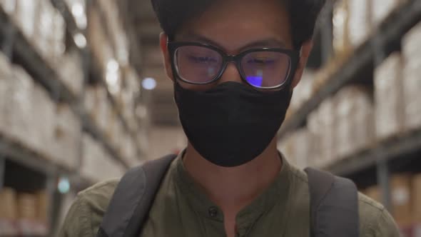 Asian man wearing mask walking in warehouse and use smart phone.