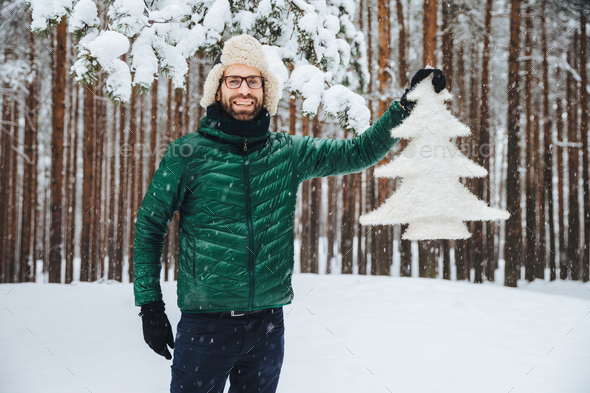 Smiling man holding a snow-covered pine tree cutout in a snowy forest