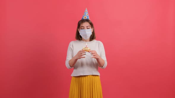 Sad Girl with Medical Mask on Her Face Tries To Blow the Candle Off the Cake alt