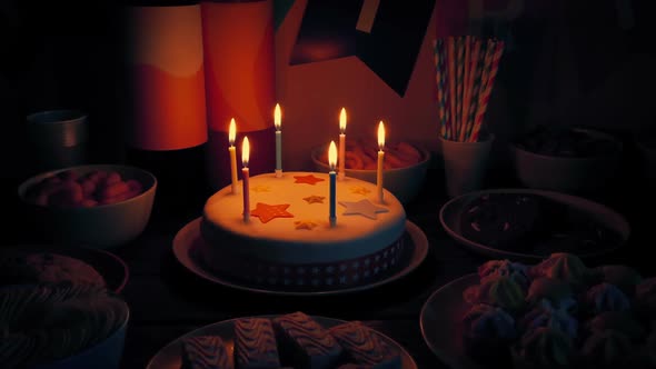Birthday Cake On Table With Snack Foods In The Dark alt