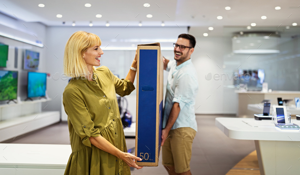 Cheerful young couple carrying packed TV they bought on sale. Tech store interior.