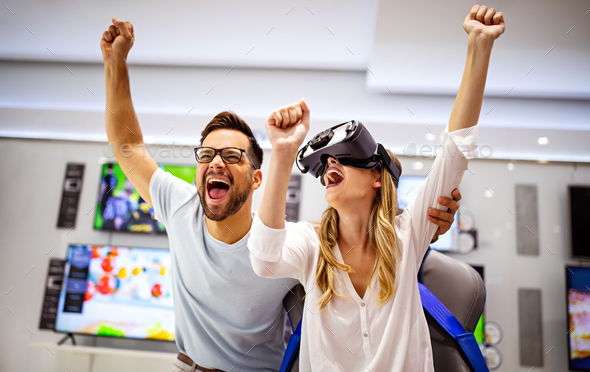Young happy couple playing video games with virtual reality glasses in technical store