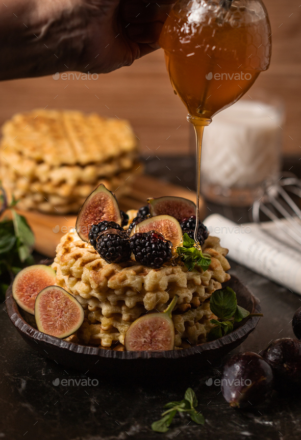 Chef\'s hand pouring honey on the Belgian waffles with figs and blackberries