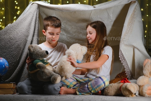 Two little children play at home in the evening to build a camping tent