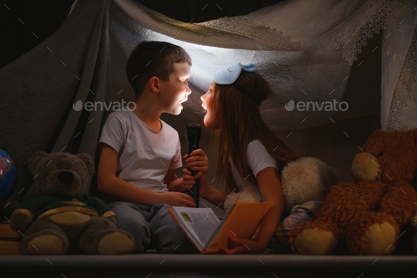 Two little child play at home in the evening to build a camping tent