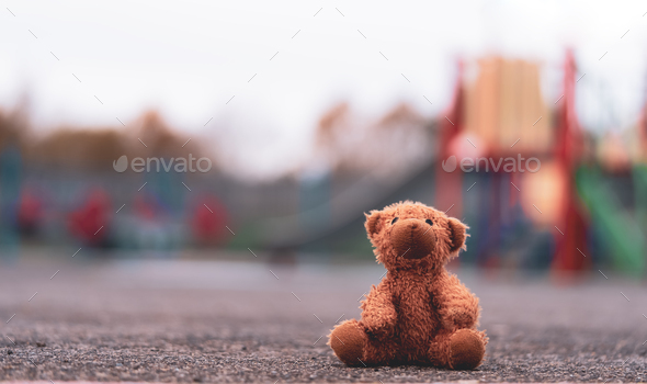 Lost teddy bear toy lying on playground floor in gloomy day,Lonely and sad brown bear doll